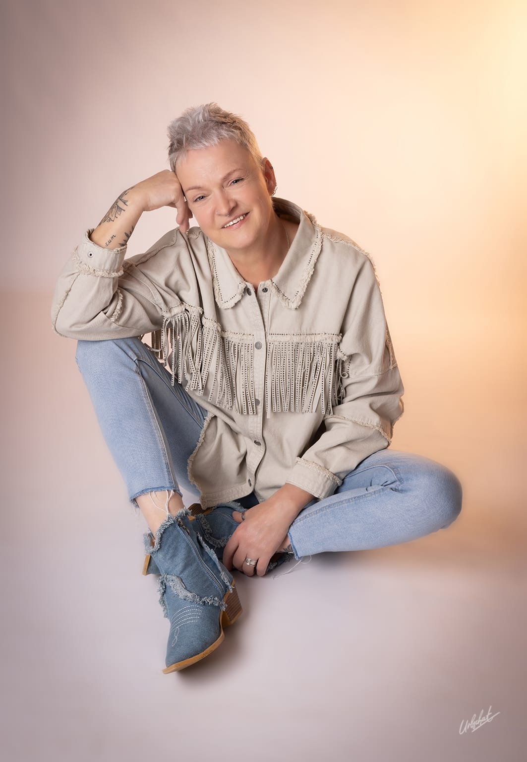Katlui — Casual look: western fringe denim jacket with distressed jeans and boots, relaxed cross-legged pose